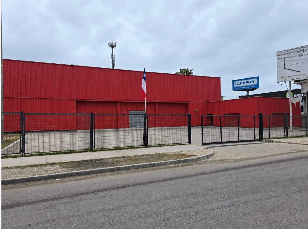 Frontis de la oficina principal con fachada roja, bandera y cierre perimetral